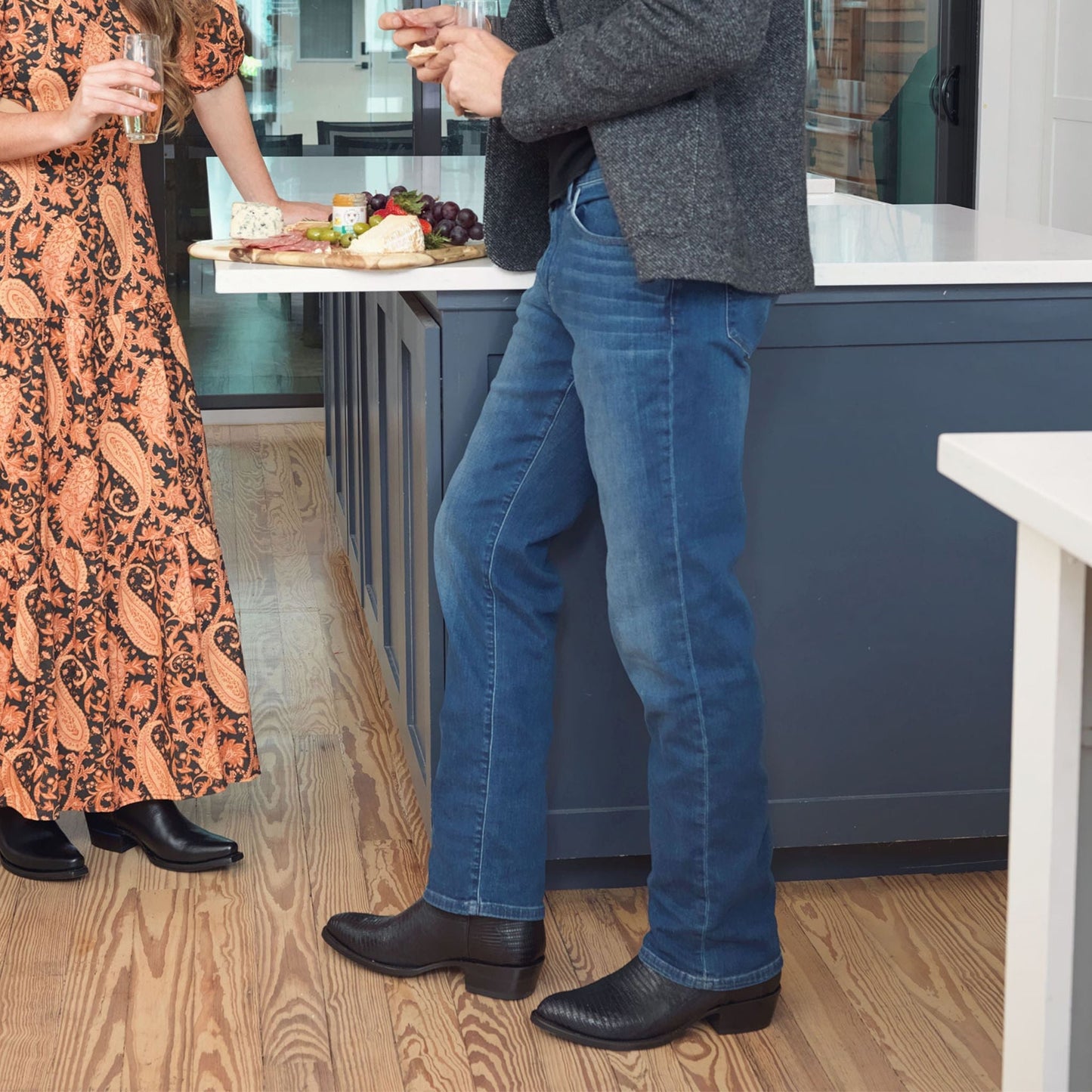 Black cowboy boots on feet with jeans, featuring stitched panels and low stacked heels.
