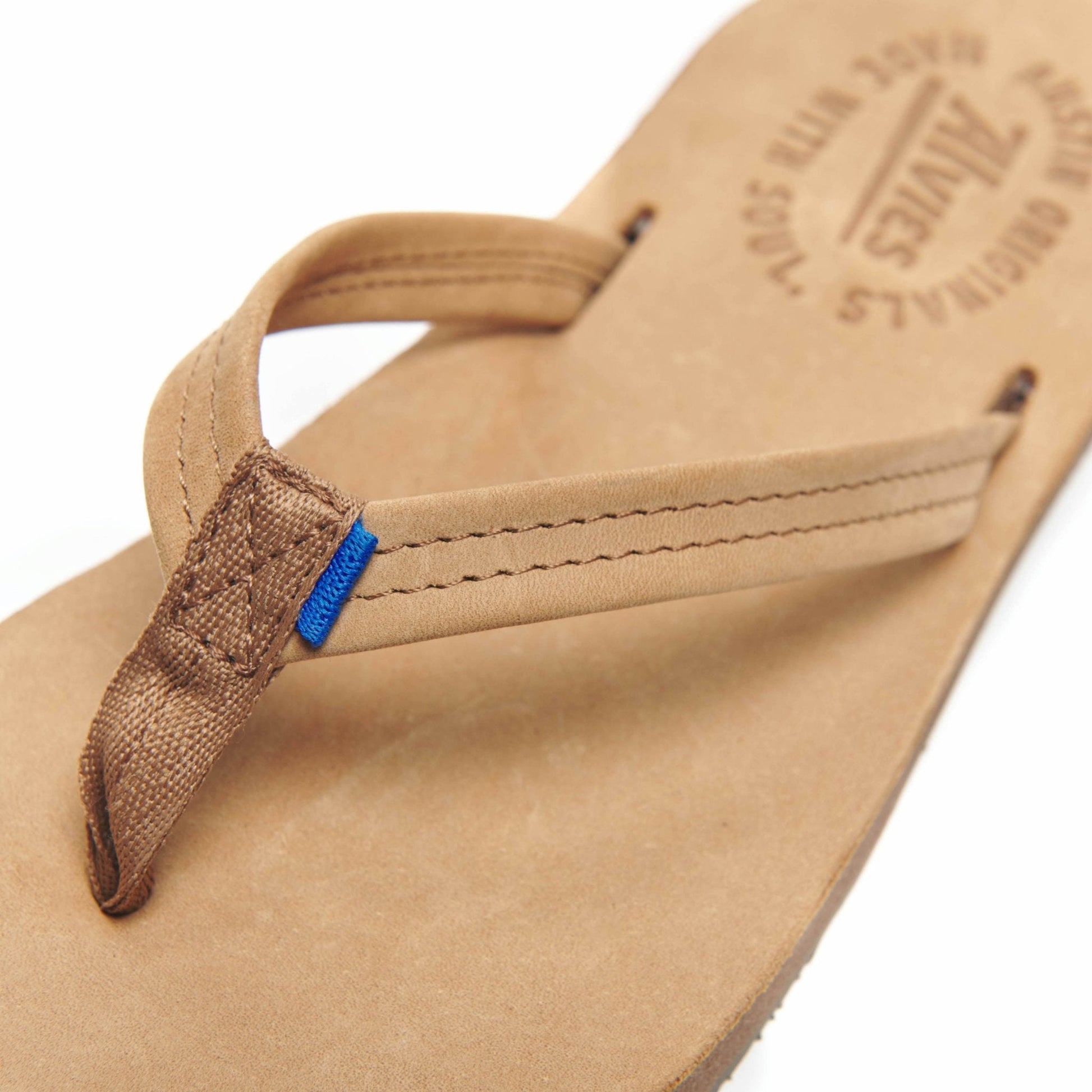 Close-up tan flip-flop with brown toe thong and blue accent tab