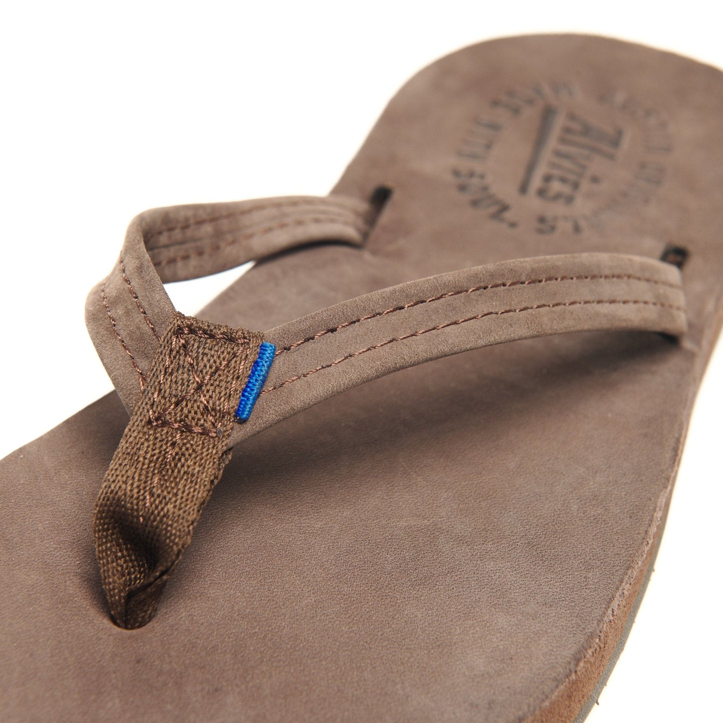 Close-up brown suede flip-flops with blue-accented thong strap and stitching