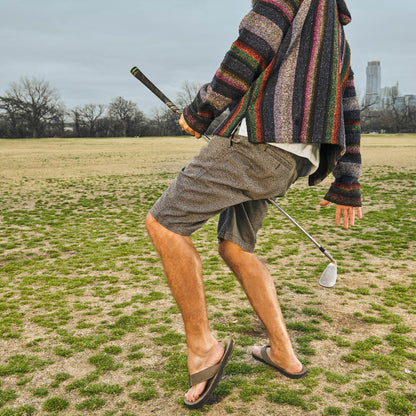 Tan shorts and gray flip-flops on an outdoor golf course, walking stance
