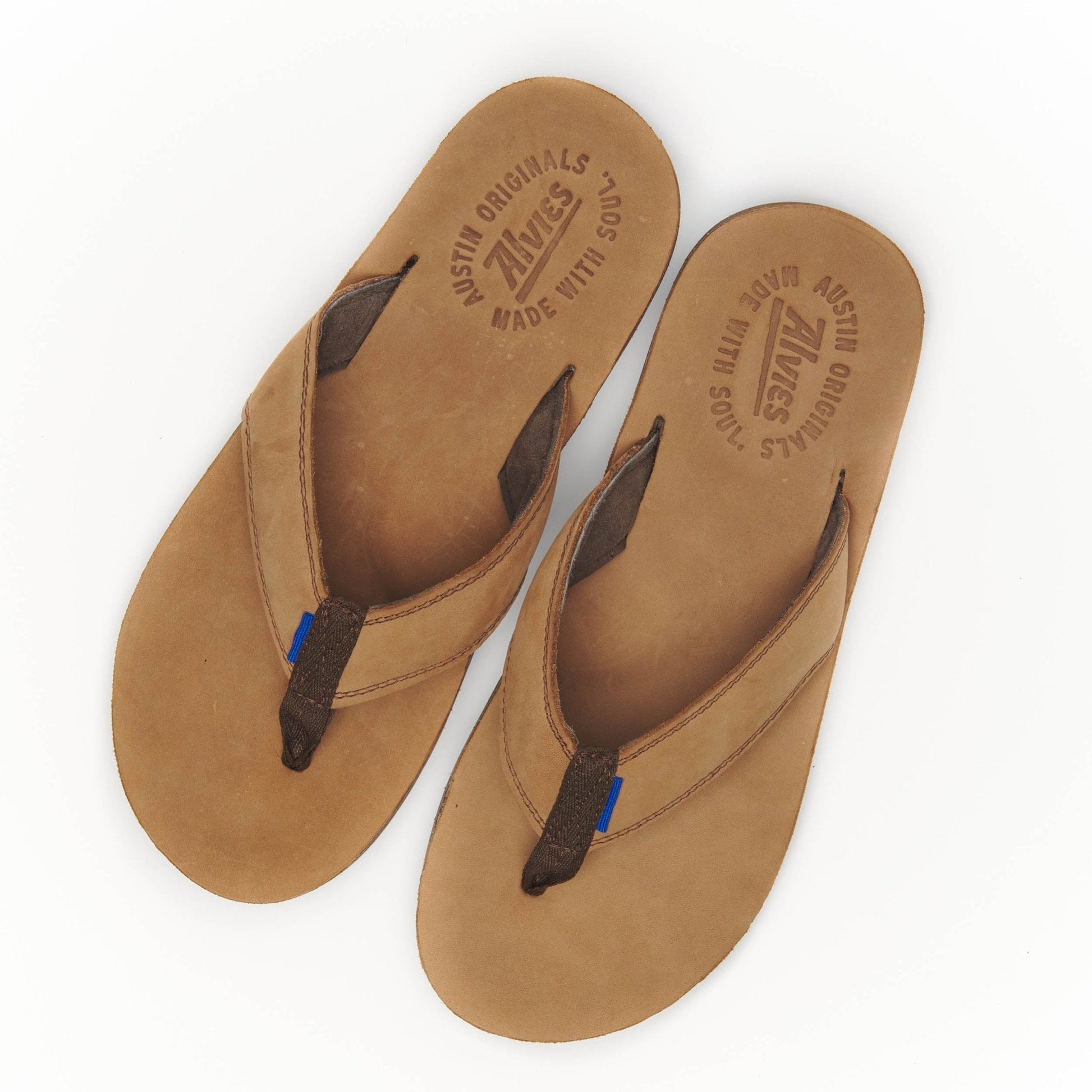 Tan suede flip-flops with embossed insole text and black thong straps.