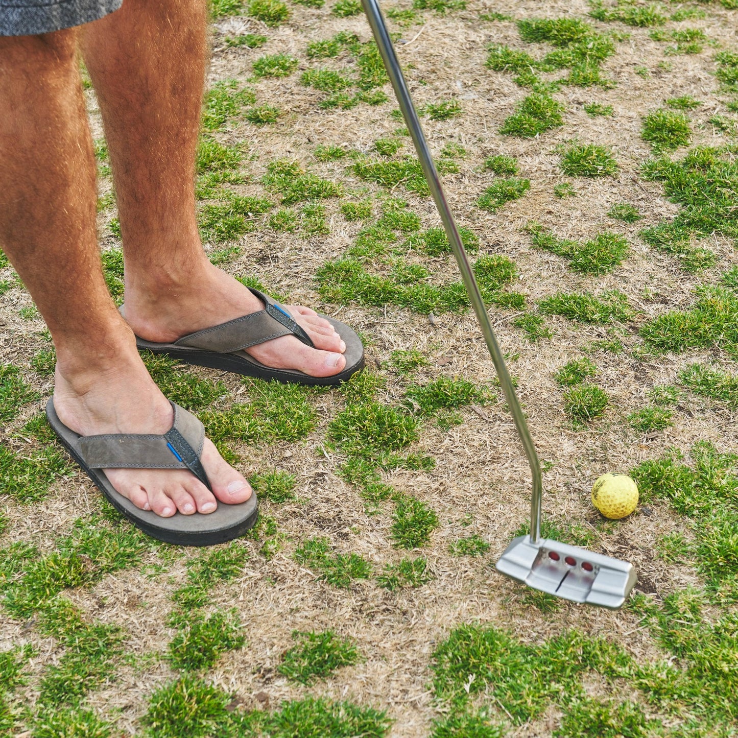 Dark flip-flops with thong straps and textured sole, worn with bare feet outdoors