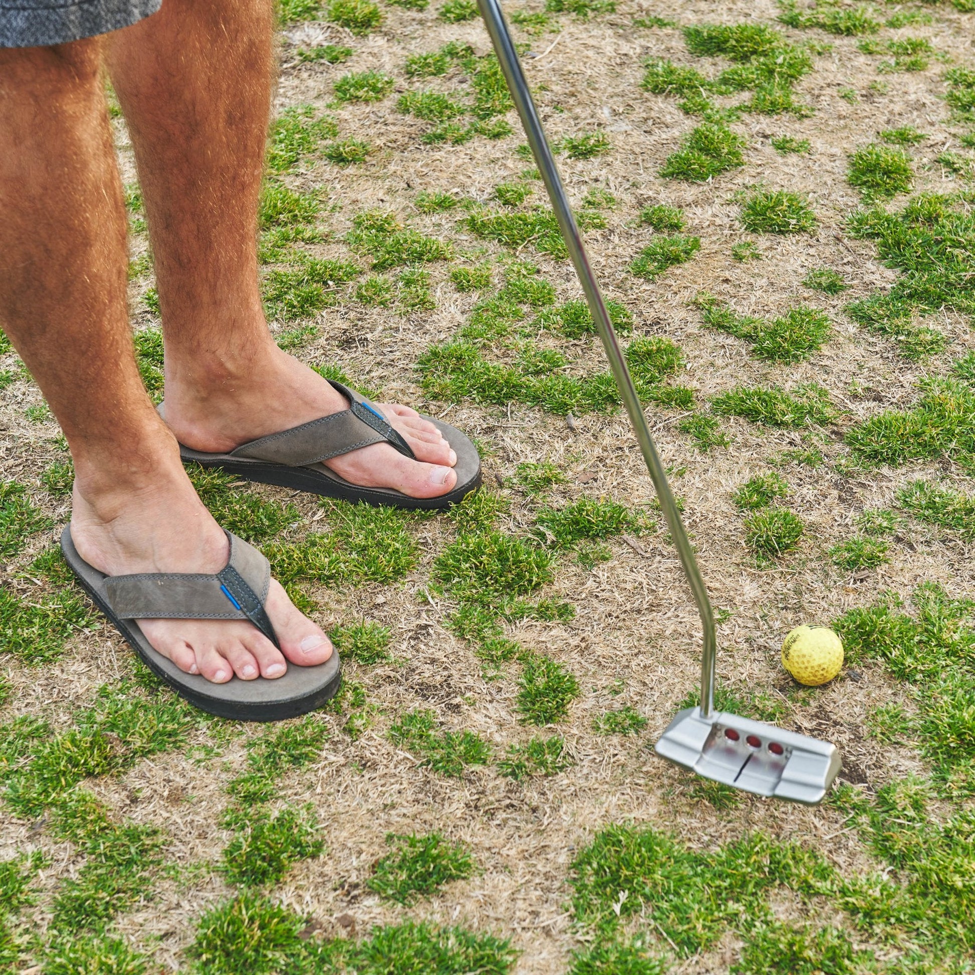 Dark flip-flops with thong straps and textured sole, worn with bare feet outdoors