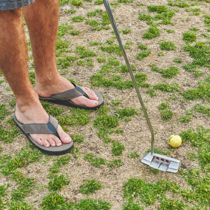 Dark flip-flops with thong straps and textured sole, worn with bare feet outdoors