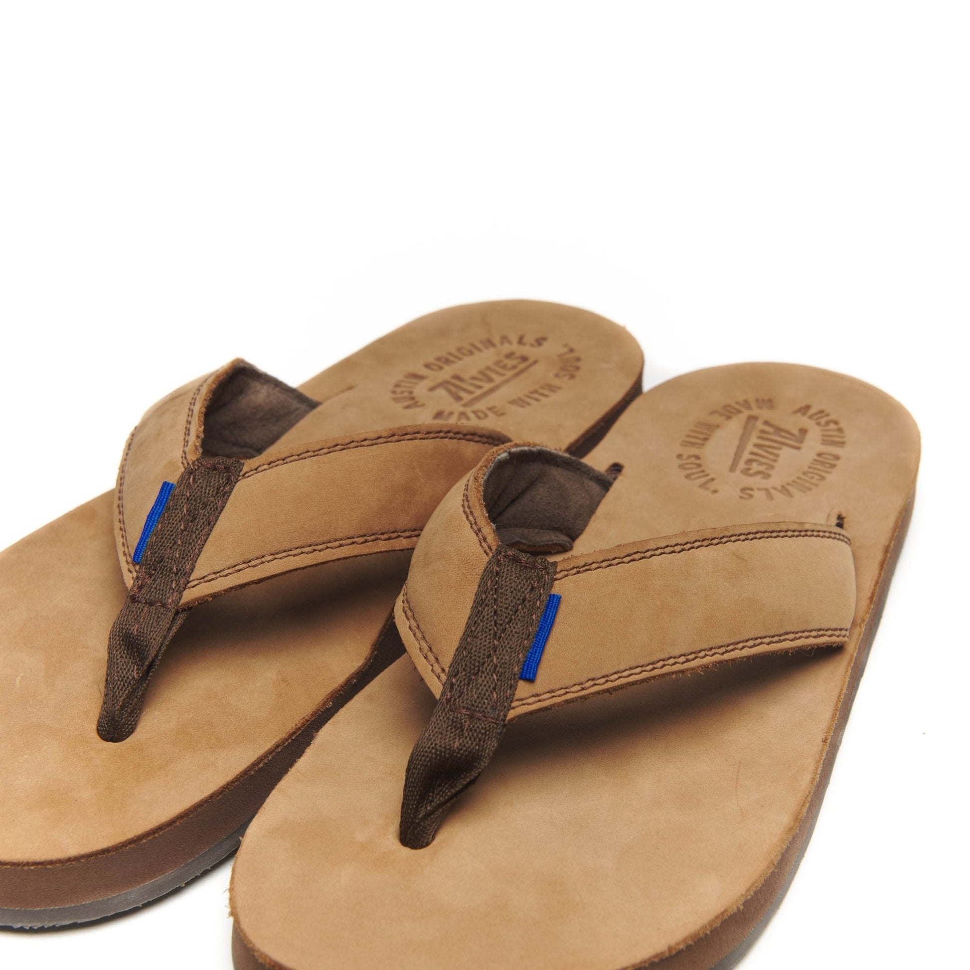 Close-up pair of tan flip-flops with dark straps and blue accent stitching
