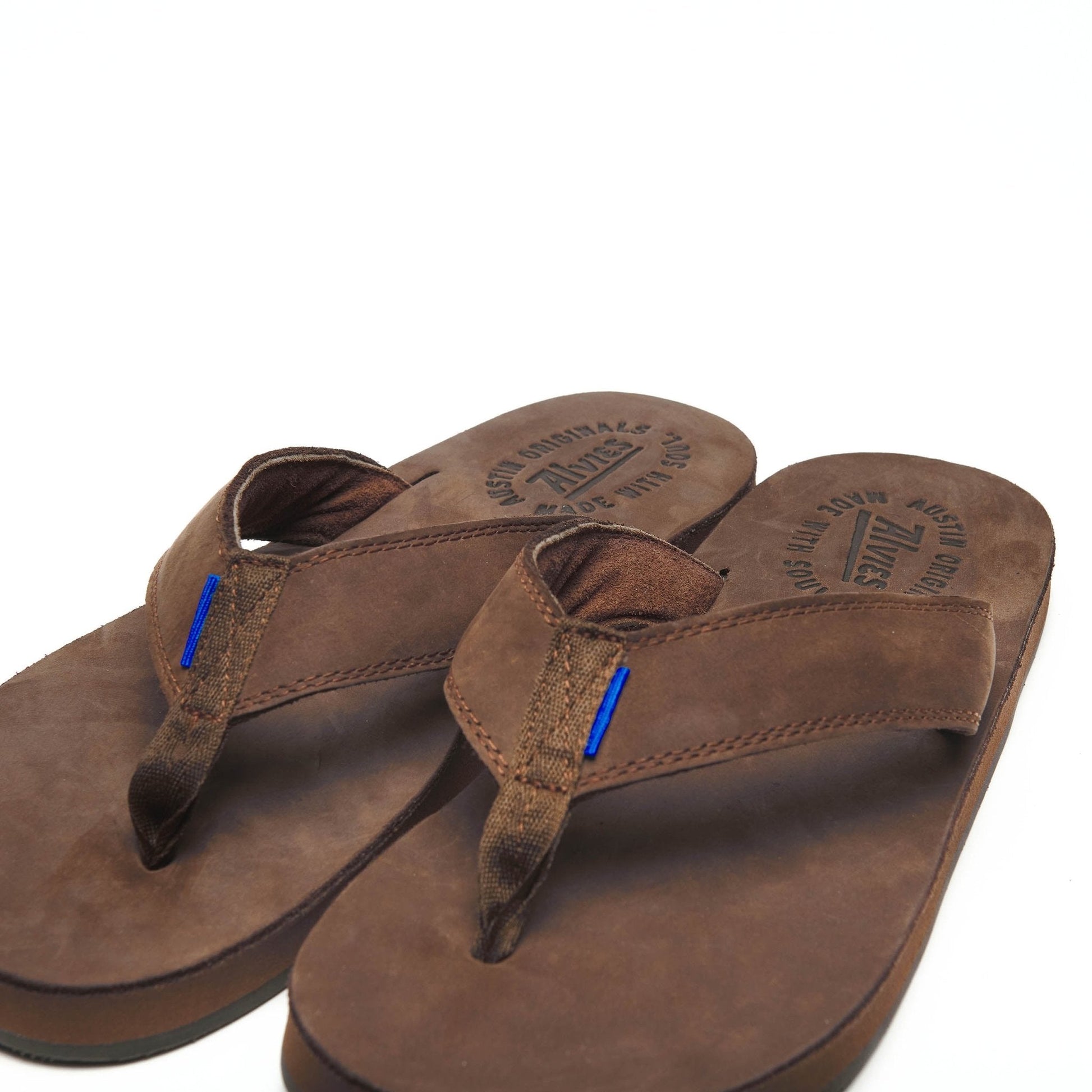 Brown suede flip-flops showing stitched straps and blue pull tabs on toe thong