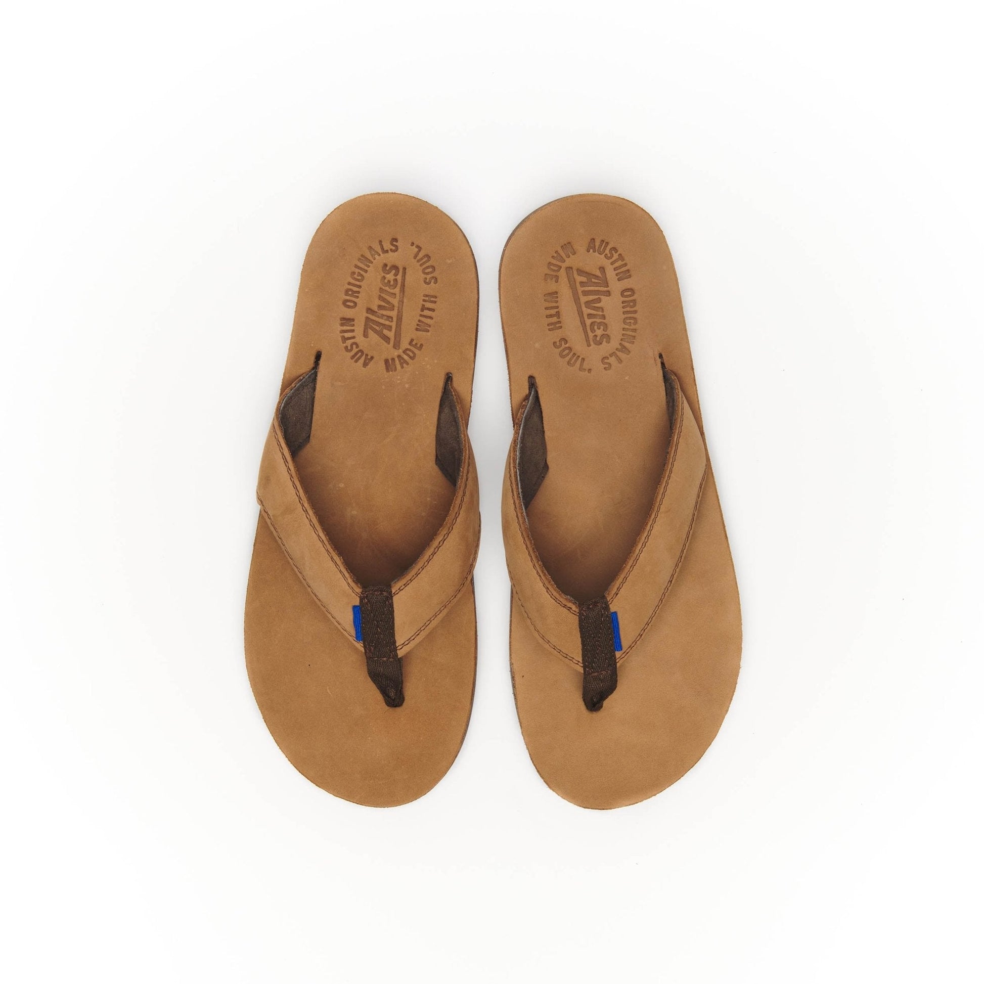 Pair of tan suede flip-flops with black thong straps and blue stitch accents.