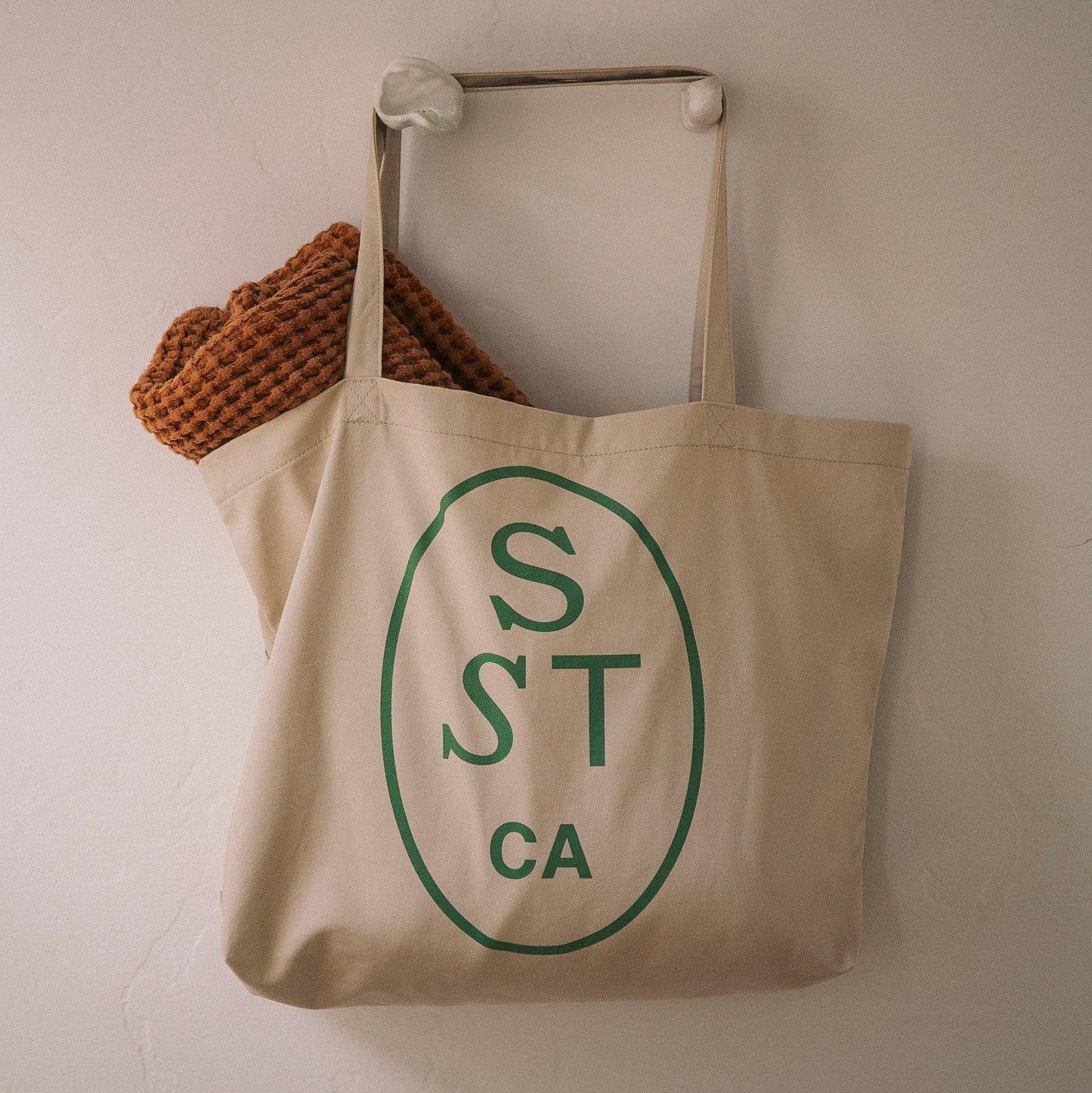 Beige canvas tote bag with long handles and green circular logo 'S ST CA'