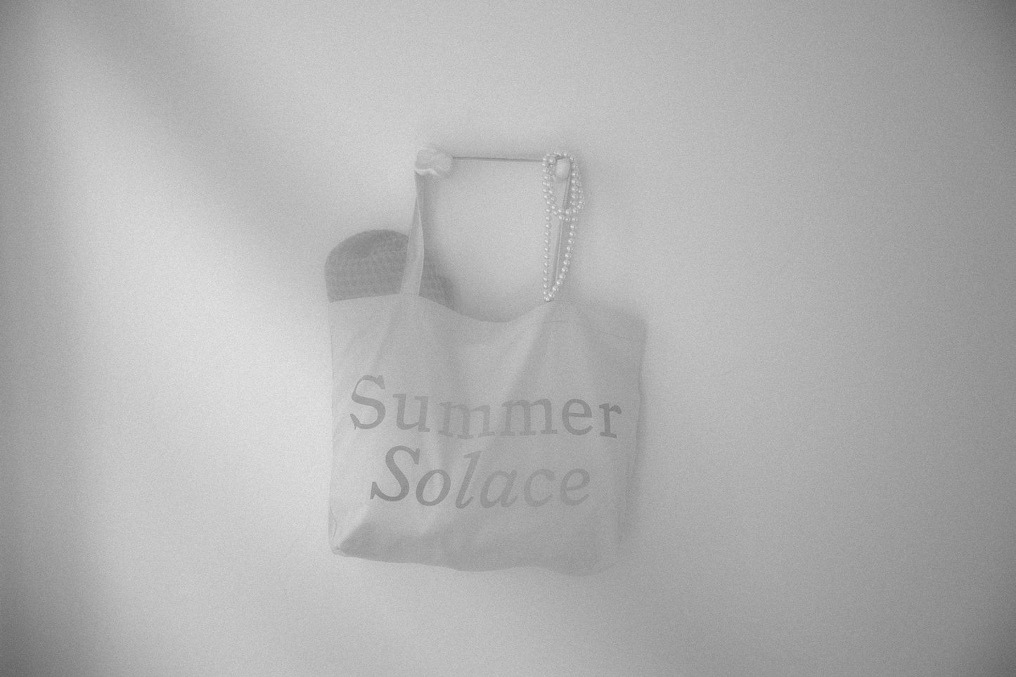 Canvas tote bag with long handles and faint 'Summer Solace' text, light gray tone