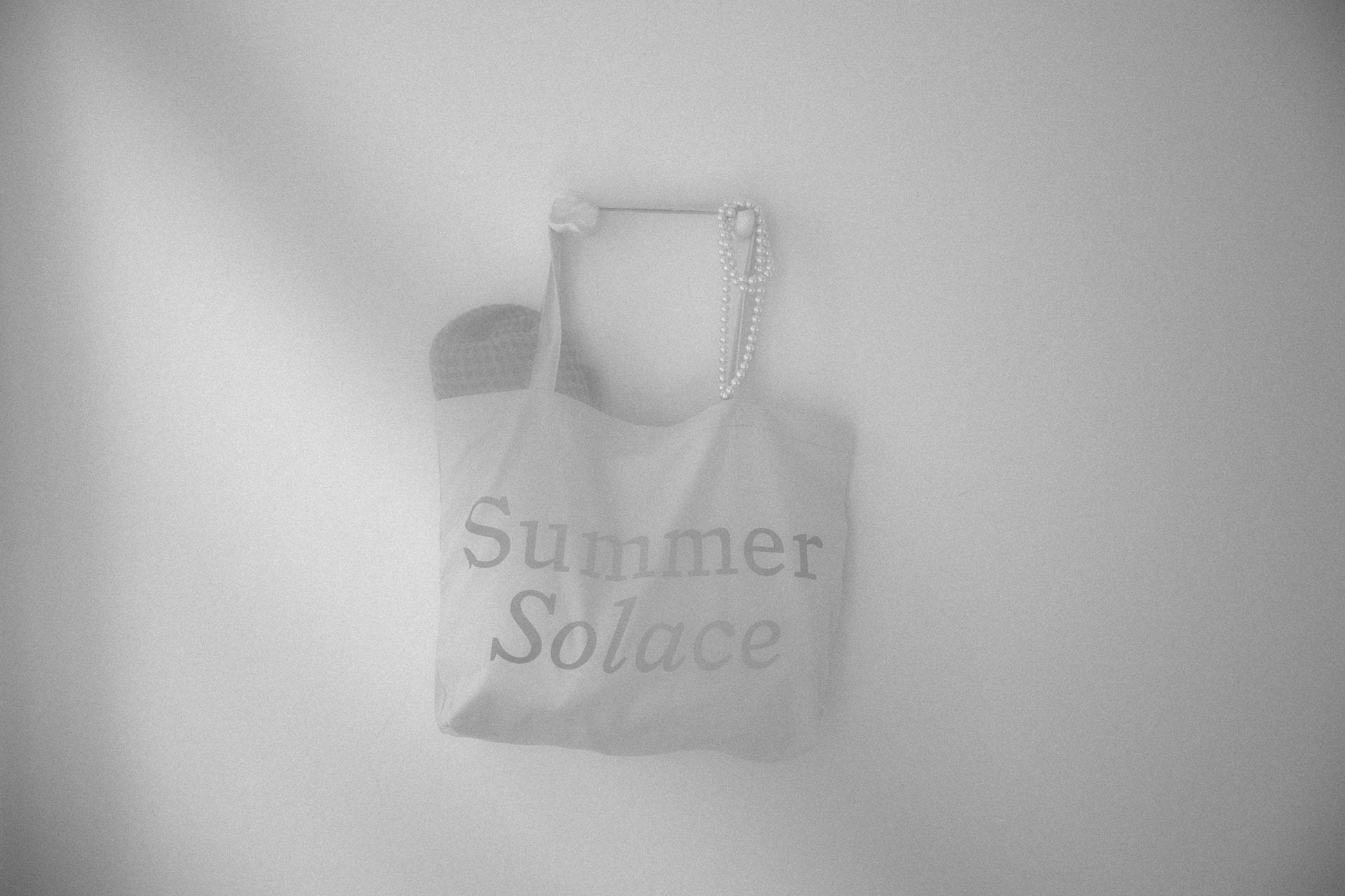 Canvas tote bag with long handles and faint 'Summer Solace' text, light gray tone