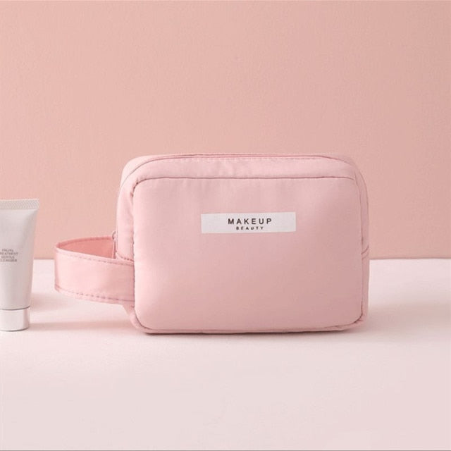 Makeup bag light pink, zip-top cosmetic pouch with front label and rounded shape.