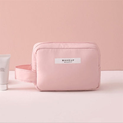 Makeup bag light pink, zip-top cosmetic pouch with front label and rounded shape.