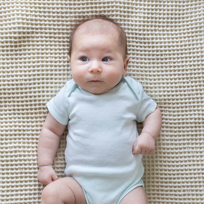 Waffle baby blanket in cream, textured surface shown behind a baby