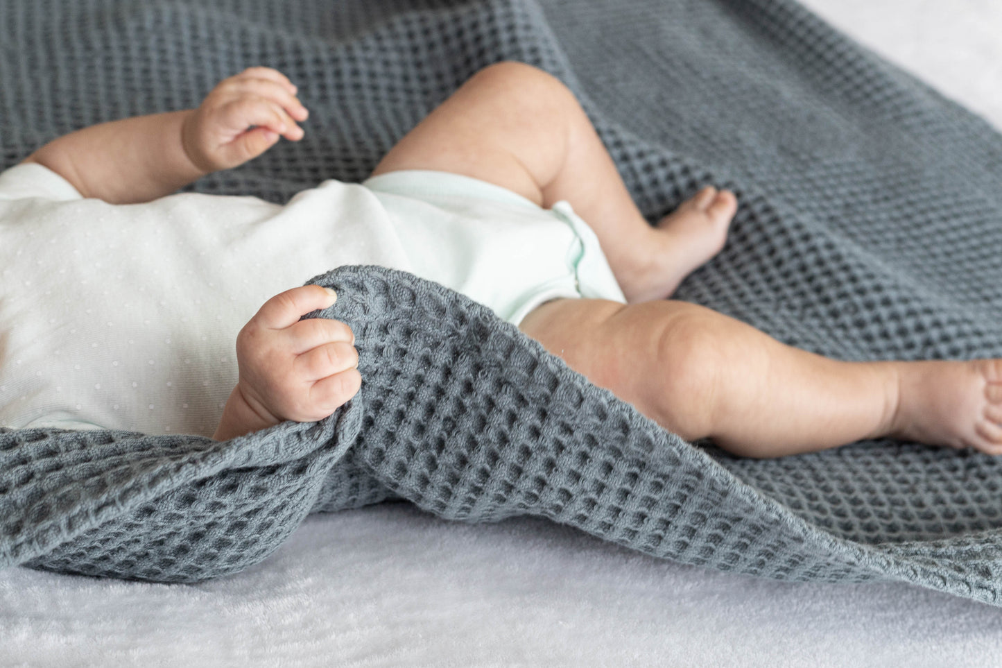 Waffle baby blanket in gray, folded and wrapped around a baby
