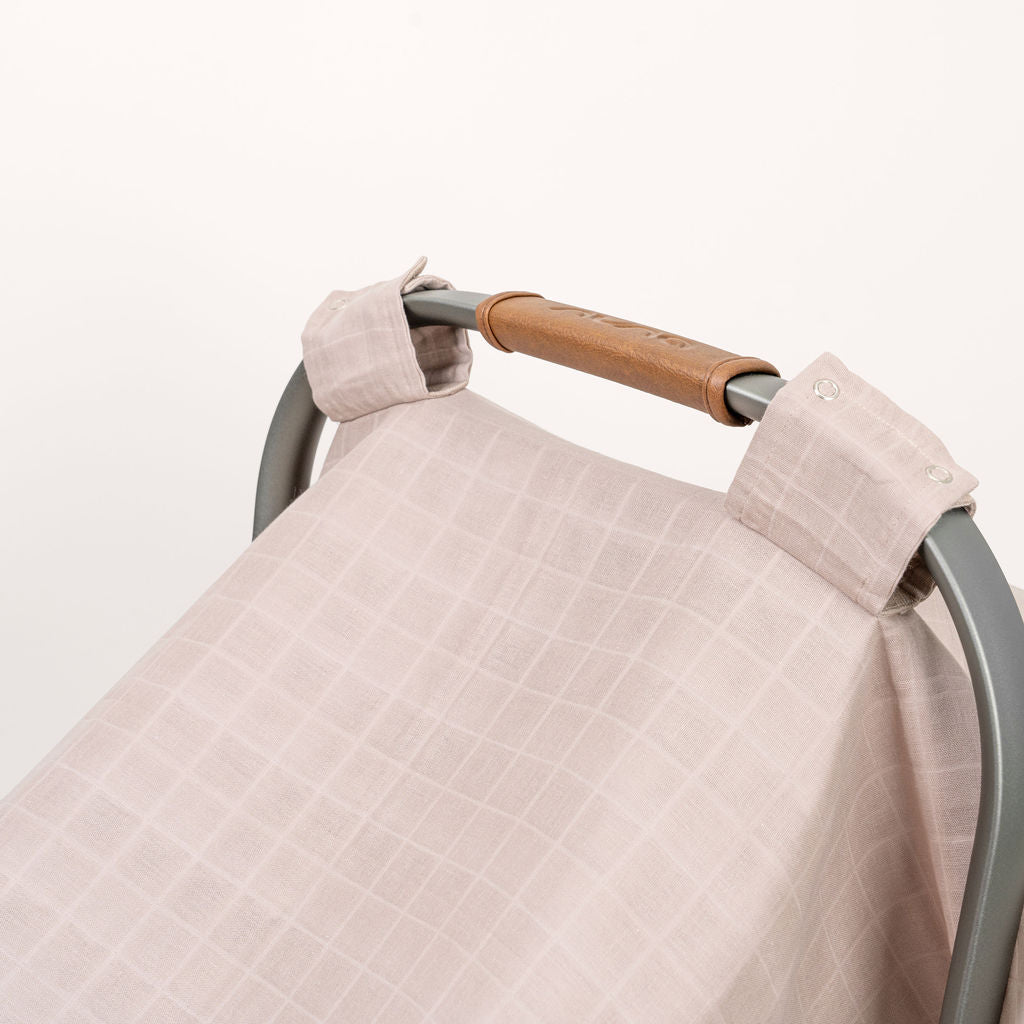 White muslin car seat cover with buttoned strap and folded corner detail
