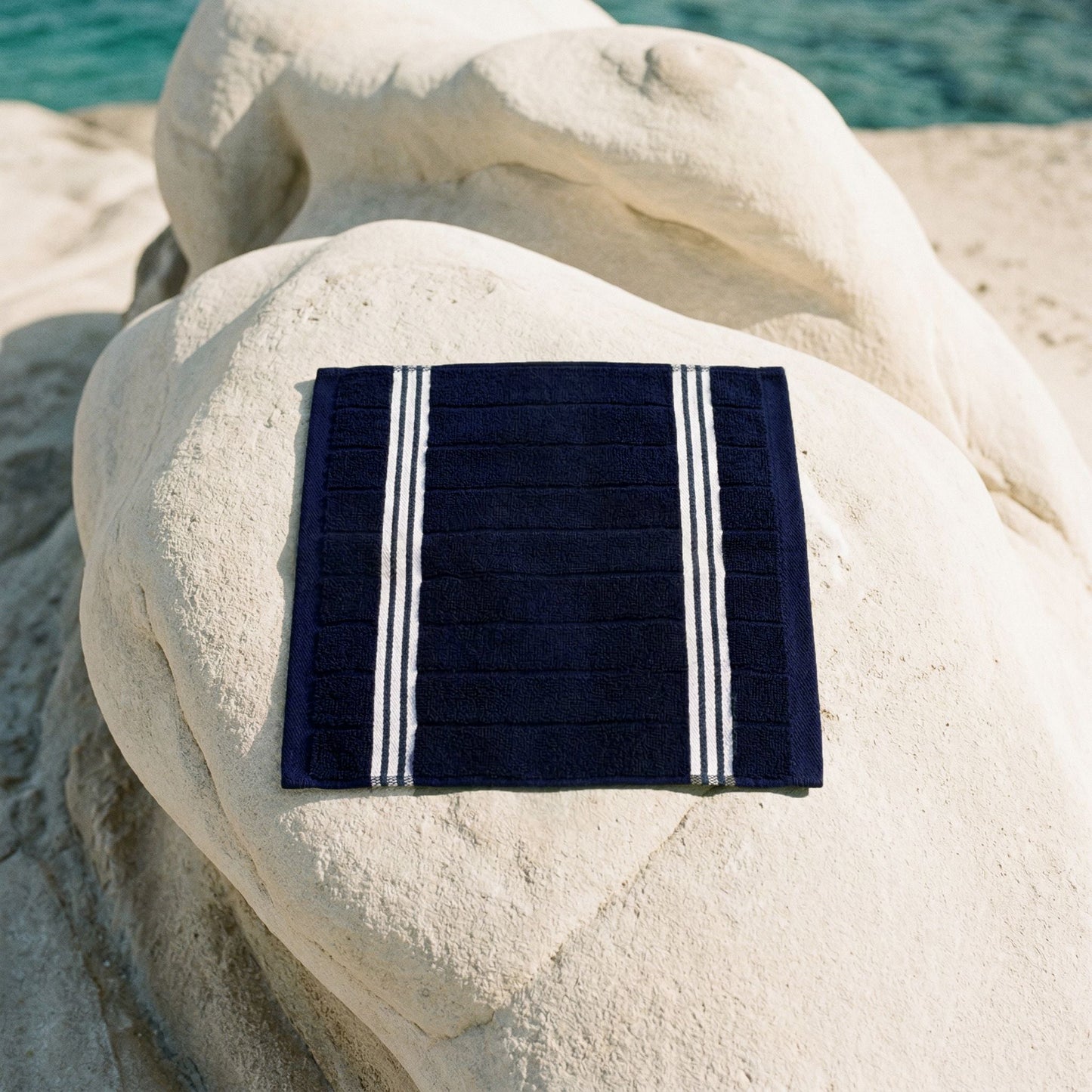 Navy cotton towel with white striped borders, folded on rocks.