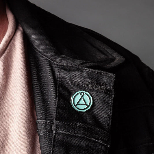 Enamel seal pin with teal octagon outline and A emblem on a dark jacket pocket