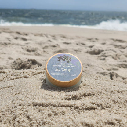 Tallow balm jar on sandy surface with blue lid label and gold lotus emblem