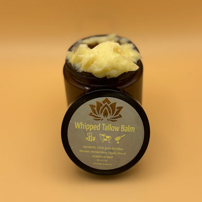 Whipped tallow balm jar with black lid and open scoop of pale yellow balm