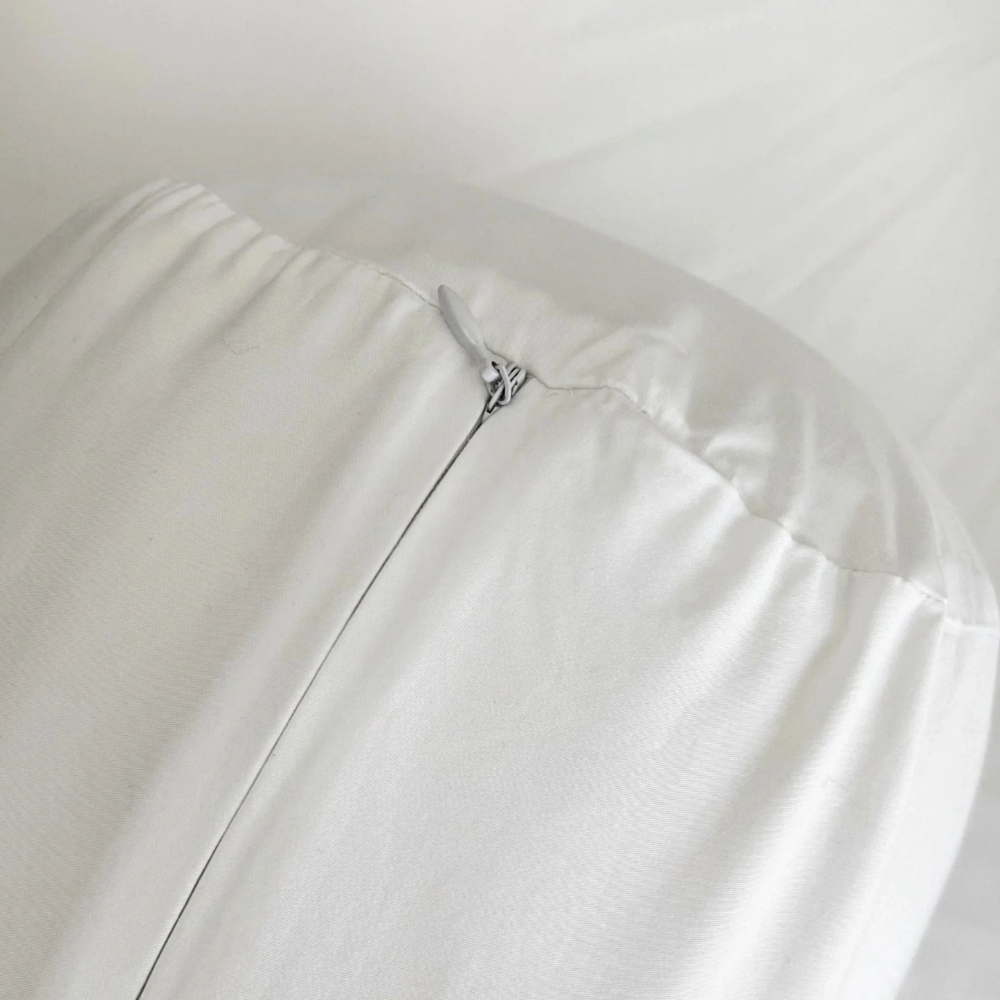 White bolster pillowcase close-up, zipper seam and metal pull tab.