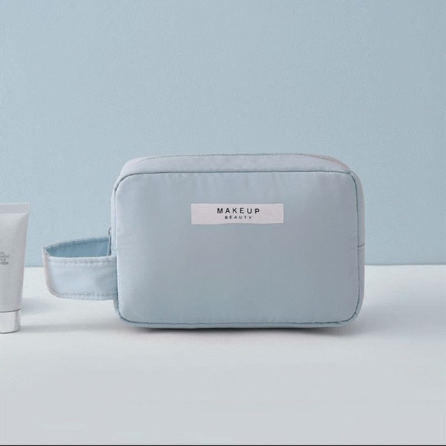 Cosmetic pouch light blue, zip-top with front label and rounded rectangular shape.