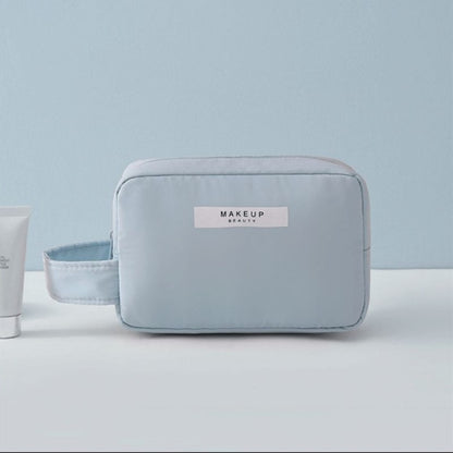 Cosmetic pouch light blue, zip-top with front label and rounded rectangular shape.